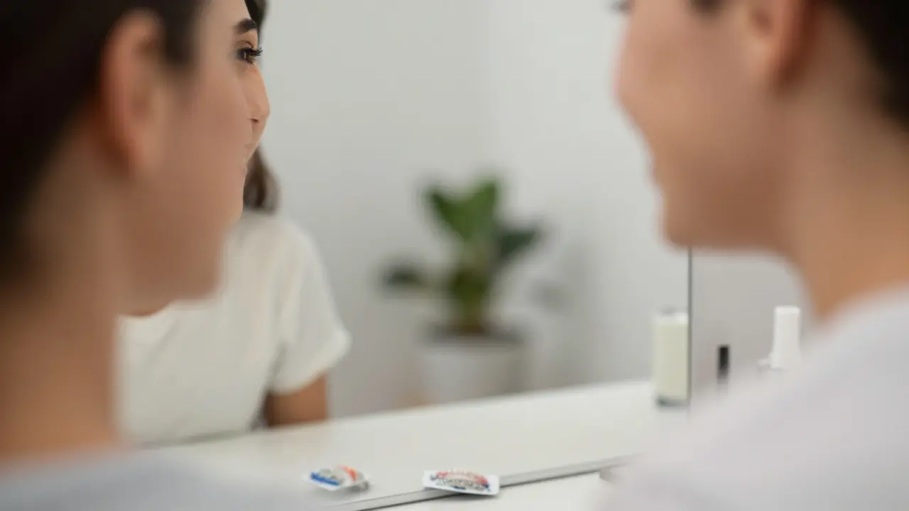 Usměvavá osoba s rovnátky se dívá do zrcadla.